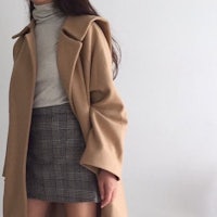 a woman wearing a camel coat and plaid skirt